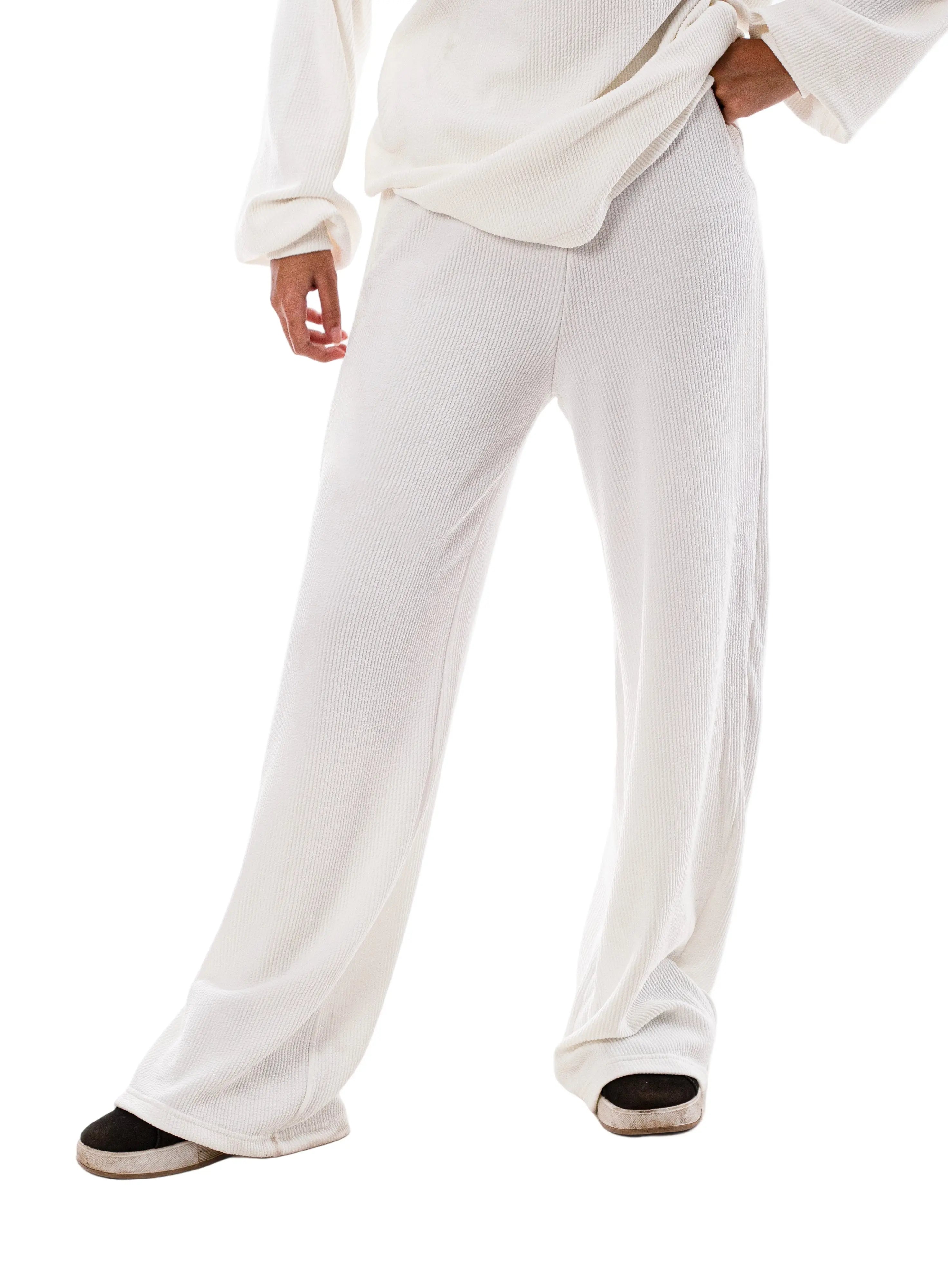 A person standing against a white background, wearing white swing pants and a matching top.