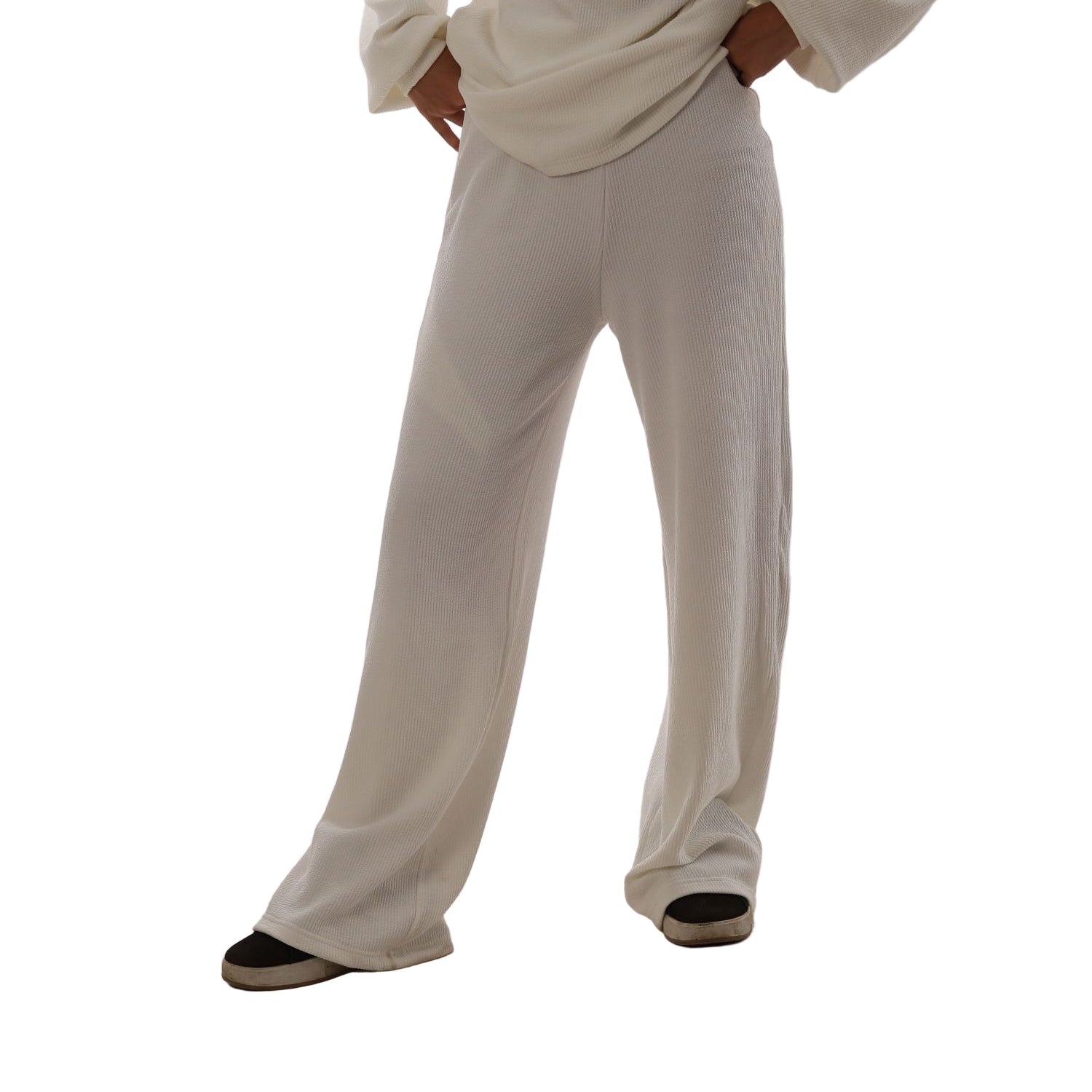 Person wearing white pants and a white hoodie against a white wall.