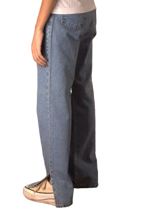 Person holding up a pair of blue jeans in front of a brown leather couch.
